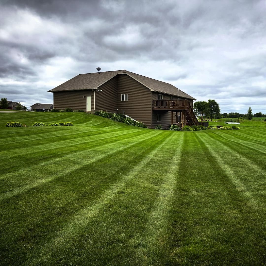 Brown house on a green lawn with striped grass and cloudy sky in the background.